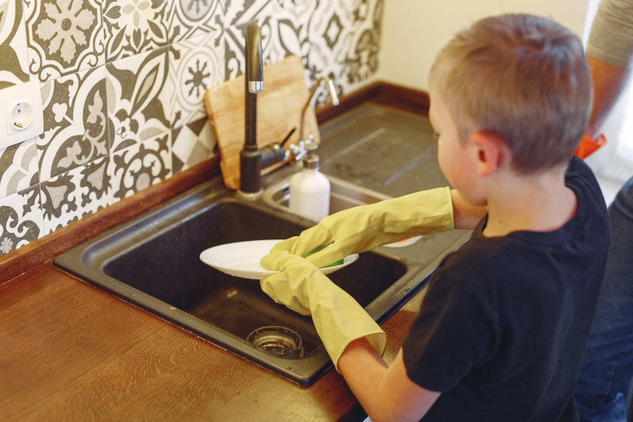 A young boy cleaning dishes at a kitchen sink, focusing on responsibility and chores.